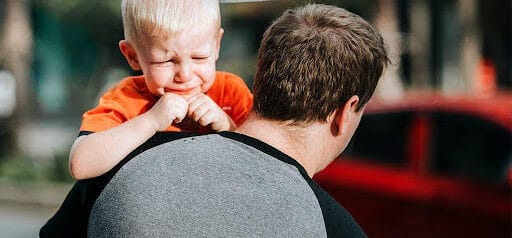 father carries toddler in arms as toddler about to cry Helland & Hurwitz Attorneys at Law Colorado