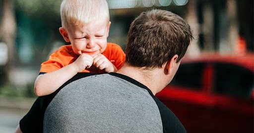 father carries toddler in arms as toddler about to cry Helland & Hurwitz Attorneys at Law Colorado