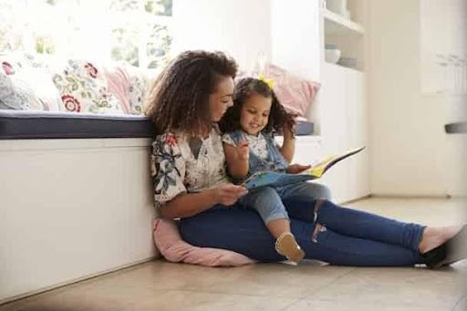 mother reads book to daughter while sitting on the floor in her home Helland & Hurwitz Attorneys at Law Colorado