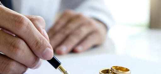 man signs prenuptial agreement while two wedding rings sit on paper Helland & Hurwitz Attorneys at Law Colorado