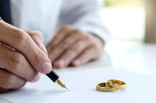 man signs prenuptial agreement while two wedding rings sit on paper Helland & Hurwitz Attorneys at Law Colorado