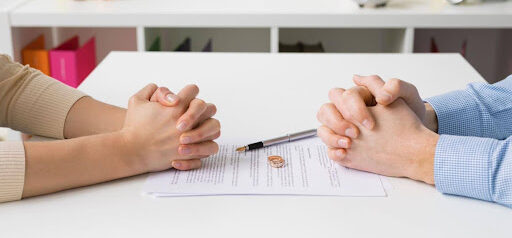 two people sit at table with hands folded with maintenance paperwork between them Helland & Hurwitz Attorneys at Law Colorado