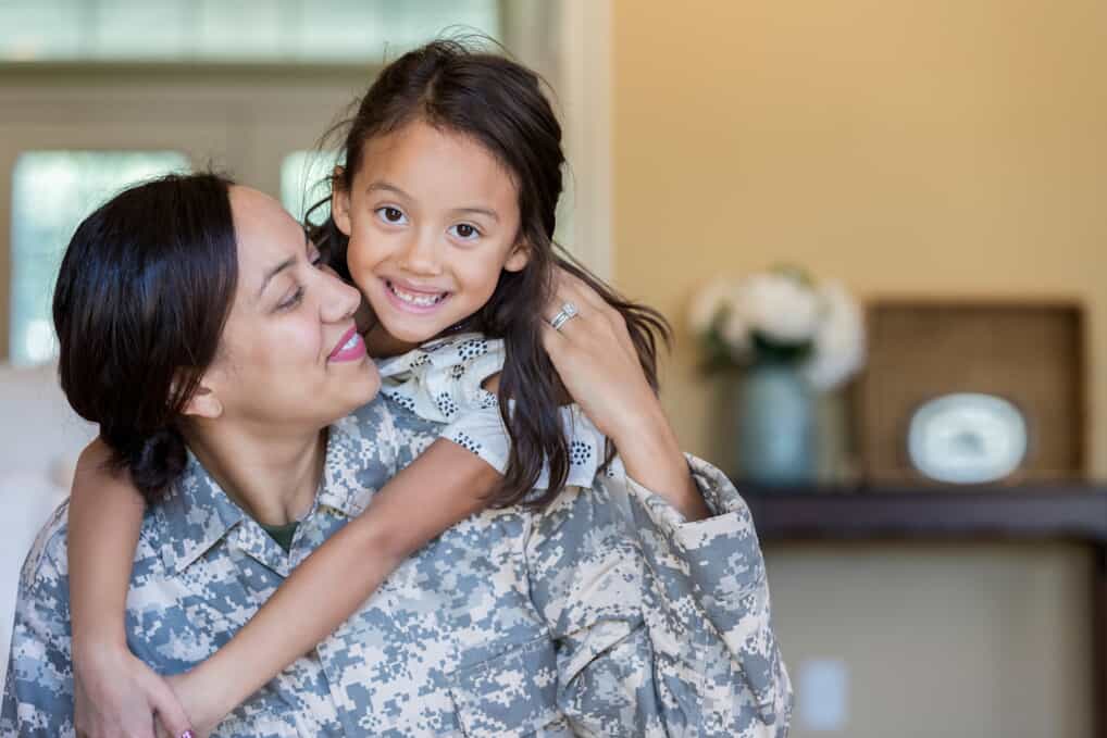 woman wearing military fatigues looks at daughter who is hugging her from her back Helland & Hurwitz Attorneys at Law Colorado