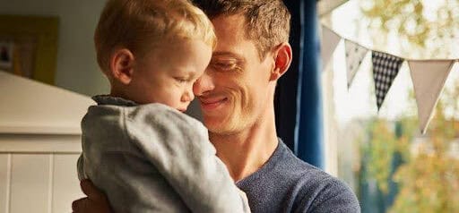 father smiles as he holds son in his arms while standing in backyard Helland & Hurwitz Attorneys at Law Colorado