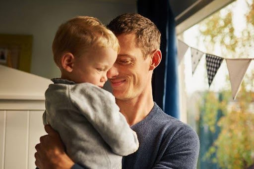 father smiles as he holds son in his arms while standing in backyard Helland & Hurwitz Attorneys at Law Colorado