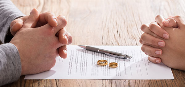 man and woman sit at table with fingers folded as they sign alimony paperwork Helland & Hurwitz Attorneys at Law Colorado