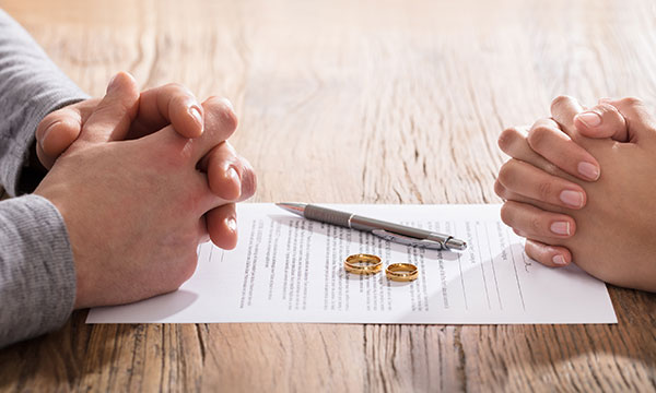 man and woman sit at table with fingers folded as they sign alimony paperwork Helland & Hurwitz Attorneys at Law Colorado
