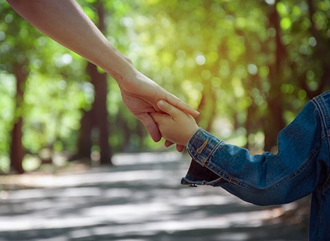 child wearing jean jacket holds parent's hands while walking down path Helland & Hurwitz Attorneys at Law Colorado