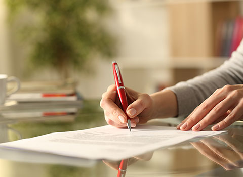 woman signs legal modification paperwork with red pen Helland & Hurwitz Attorneys at Law Colorado