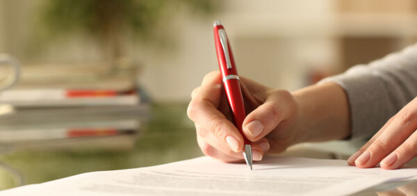 woman signs legal modification paperwork with red pen Helland & Hurwitz Attorneys at Law Colorado