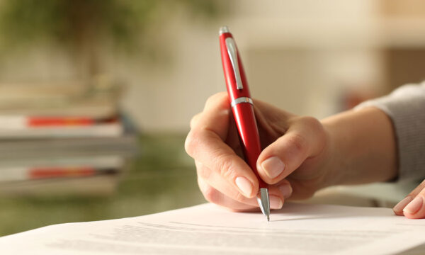 woman signs legal modification paperwork with red pen Helland & Hurwitz Attorneys at Law Colorado